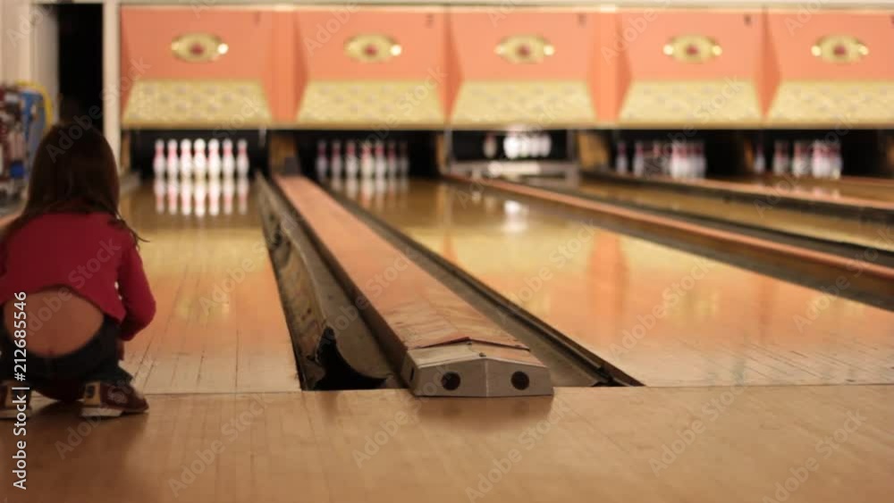 A little girl runs up the the edge of the lane and pushes her bowling ball down. A little girl runs up the the edge of the lane and pushes her bowling ball down.