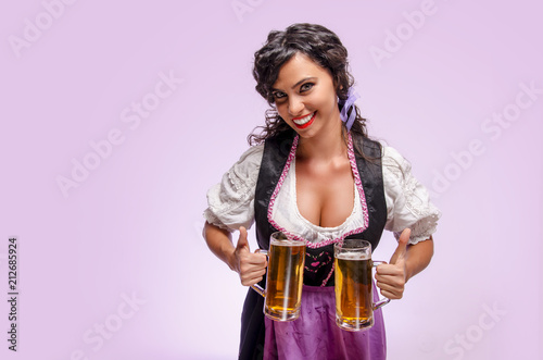 Attractive young woman in Bavarian traditional clothes with two beer mugs, studio shot, Oktoberfest 