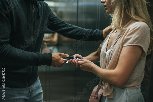 cropped view of robber attacking woman and stealing smartphone in elevator