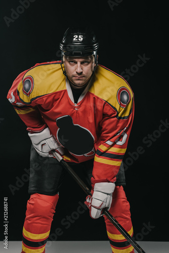Photography professional ice hockey player holding hockey stick and looking at camera on bla
