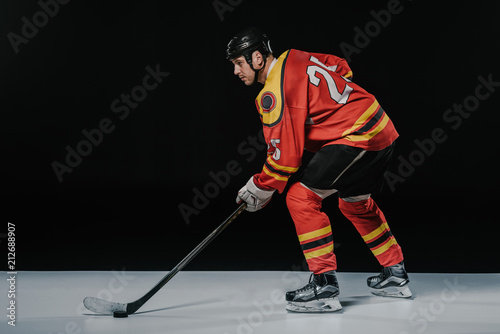side view of professional young ice hockey player playing hockey and looking away on black photo