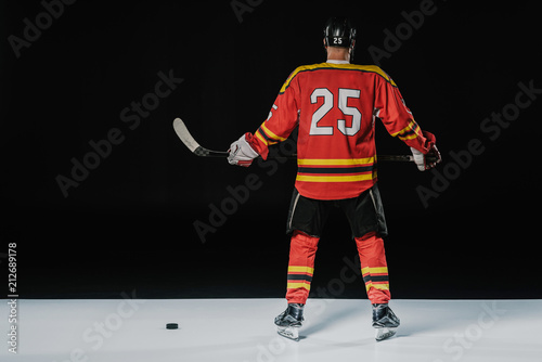 Fototapeta Naklejka Na Ścianę i Meble -  back view of professional ice hockey player holding hockey stick on black