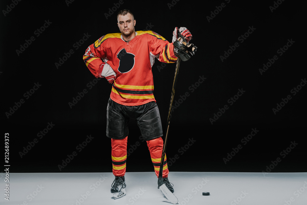 Fototapeta premium full length view of professional ice hockey player standing with hand on waist and looking at camera on black