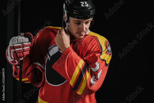professional adult hockey player holding hockey stick and wearing helmet isolated on black
