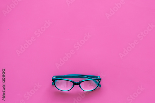 One glasses with transparent lenses on pink background top view copy space