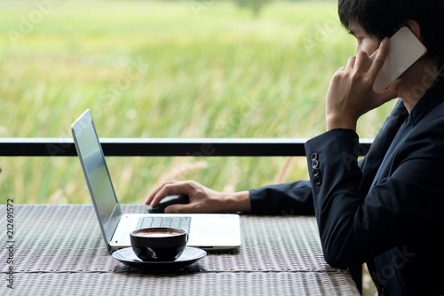 business man sitting at table in coffee shop. On table is laptop, smartphone and cup of coffee