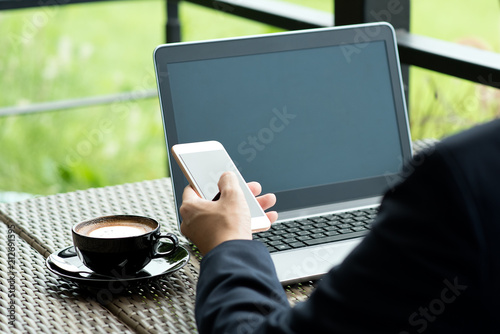 business man sitting at table in coffee shop. On table is laptop, smartphone and cup of coffee