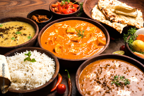 Assorted indian food for lunch or dinner, rice, lentils, paneer, dal makhani, naan, chutney, spices over moody background. selective focus 