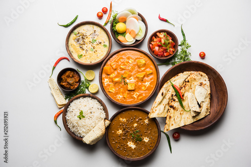 Assorted indian food for lunch or dinner, rice, lentils, paneer, dal makhani, naan, chutney, spices over moody background. selective focus
