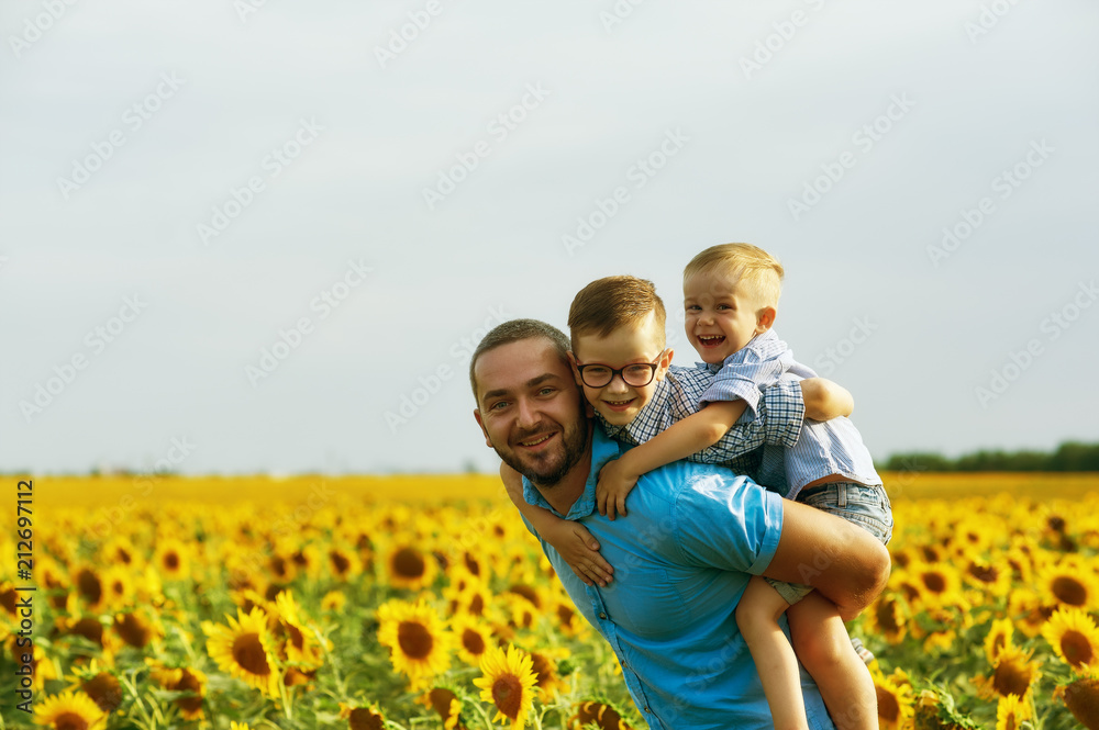 Cheerful father with his sons on vacation in the field with sunflowers . The parent plays with his son . Father's day Cheerful father with his sons on vacation in the field with sunflowers . The parent plays with his son . Father's day