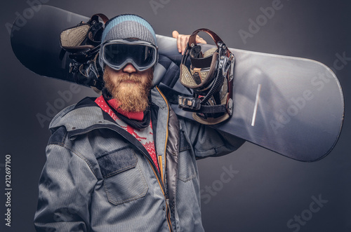 Billede på lærred Portrait of a snowboarder dressed in a full protective gear for extream snowboarding posing with a snowboard on his shoulder at a studio