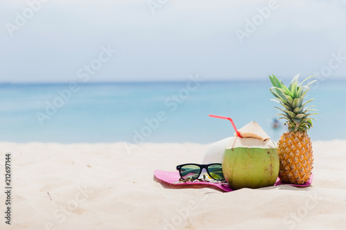 Fresh young coconut and pineapple lying on the sand beach background with straw ready for drink. Tropical vacation travel concept