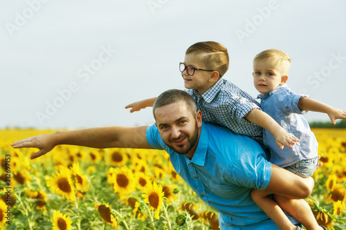 Cheerful father with his sons on vacation in the field with sunflowers . The parent plays with his son . Father's day