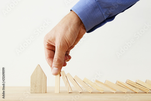 concept image of real estate insurance and protection. man hands blocking the domino effect, saving a small house