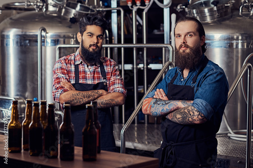 Two interracial hipster full bearded males in a  shirts and aprons working in the brewery.