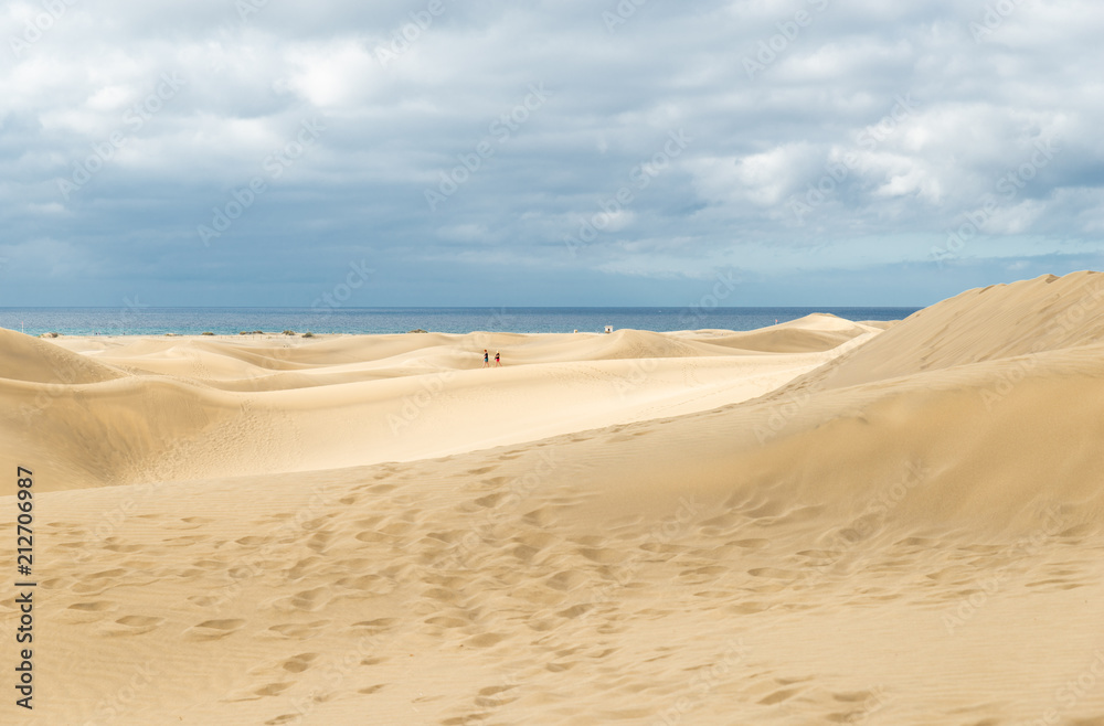 View of Dunes in Maspalomas, Canarias islands, Spain. Yellow and golden sand from Sahara desert and distance view of blue Atlantic ocean and beach.