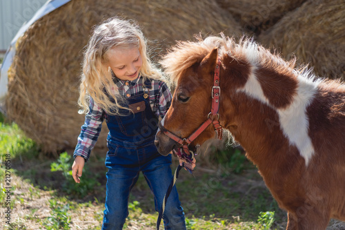 happy kid standing near cute pony at farm