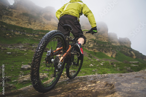 Legs of bicyclist and rear wheel close-up view of back mtb bike in mountains against background of rocks in foggy weather. The concept of extreme sports photo