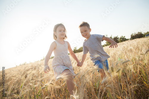 Children go to the field of wheat. A boy and a girl holding hands laugh and have fun.