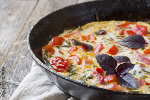 Omelet with vegetables in a pan close-up. Wooden background, top view horizontal