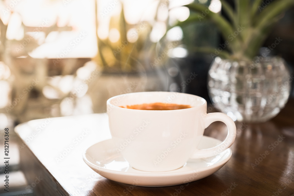 Obraz premium hot coffee in the white cup on wooden table. Sun light in cafe.