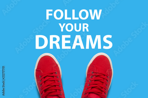 Female legs in red sneakers standing on a blue background with text Follow your dreams. Сoncept of the call to achieve their desires and dreams. Flat lay, top view