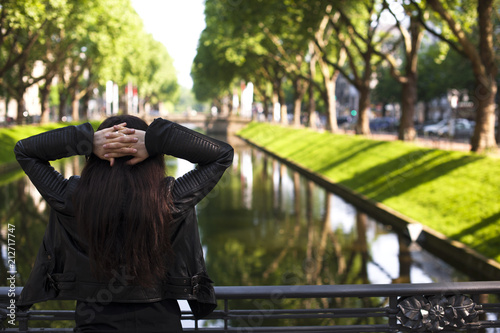The girl is posing on the avenue by the river in the city, green trees. TOURISM AND TRAVEL.Copy space.