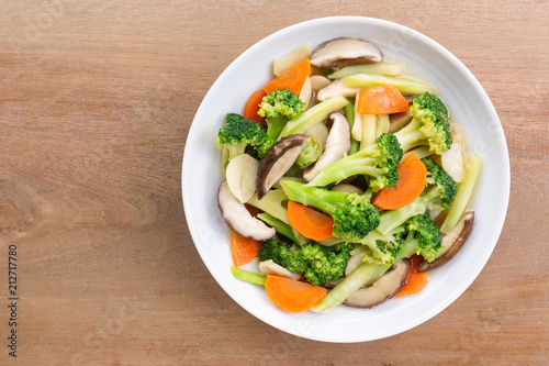 top view of stir fried vegetable with soy sauce in a ceramic dish on wooden table. homemade style food concept.