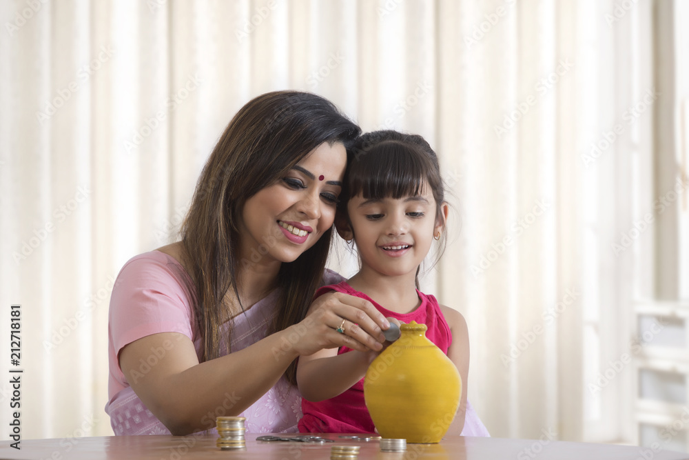Fototapeta premium Mother and daughter filling piggy bank