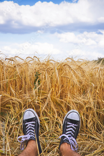 Happy summer. Man wearing black and white canvas shoes and laying in golden barley field. 