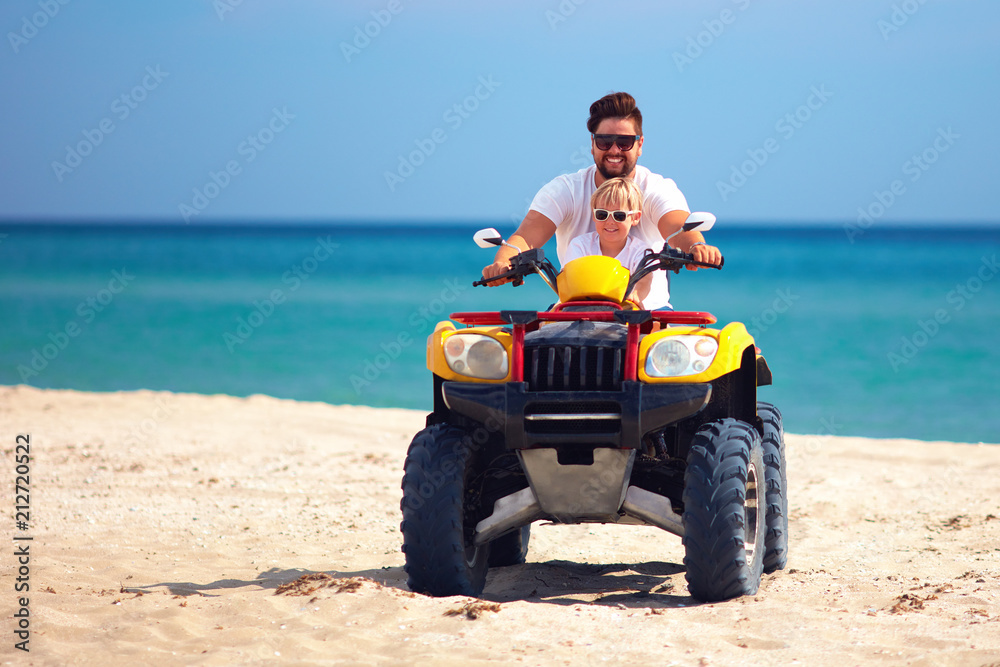 Naklejka premium szczęśliwa rodzina, ojciec i syn jedzie na quadzie atv rower na piaszczystej plaży