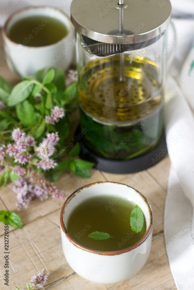 Mint tea in a clear glass teapot, mint leaves and tea cups.