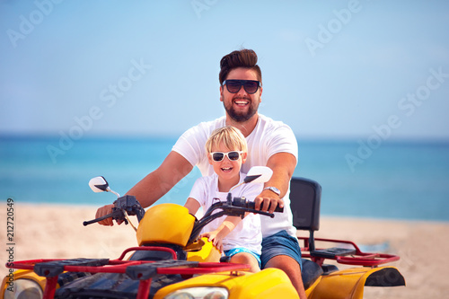 happy family, father and son riding on atv quad bike at sandy beach © Olesia Bilkei