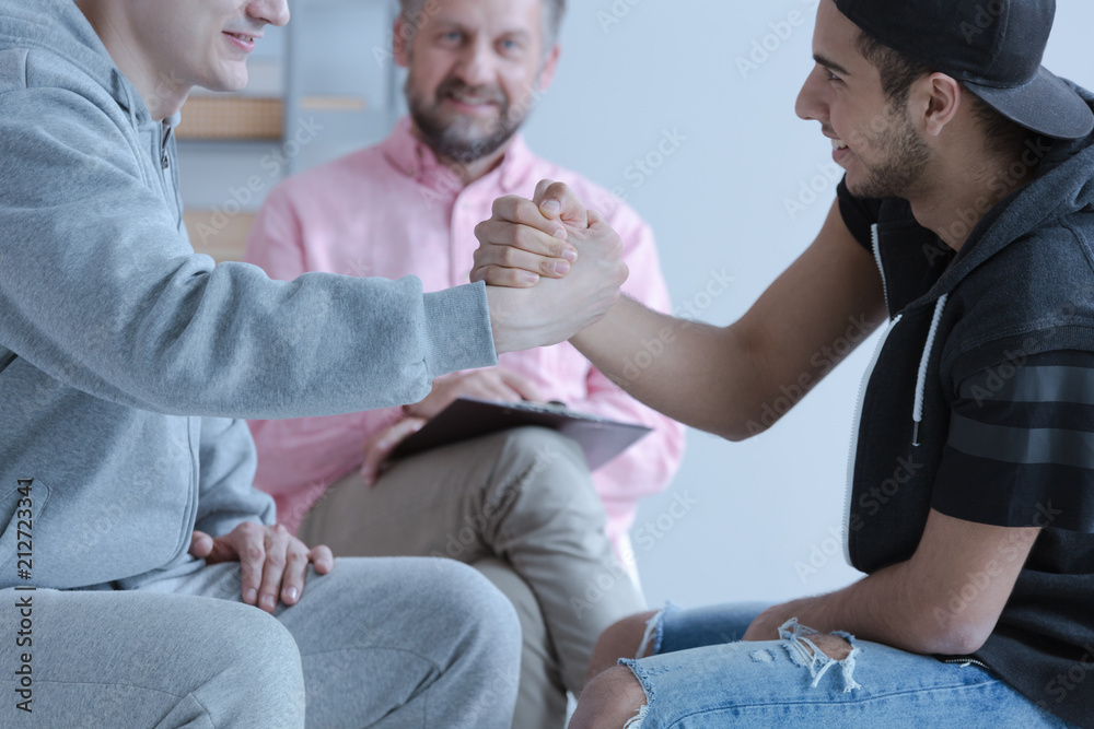 Two young man holding hands as a gesture of friendship during a mediation meeting - obrazy, fototapety, plakaty 