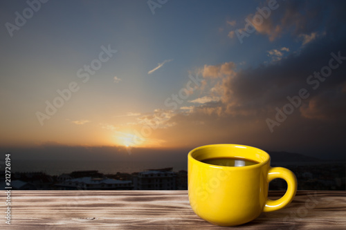 Coffee or tea in yellow cup on the wooden table opposite beautiful sunset over Mediterranean sea for background. Turkey in autumn. Alanya. Natural background. View from the roof of skyscraper