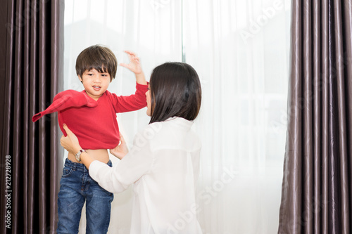 Mother dressed her baby before going to school in the morning.Mother helping son put on the shirt. photo