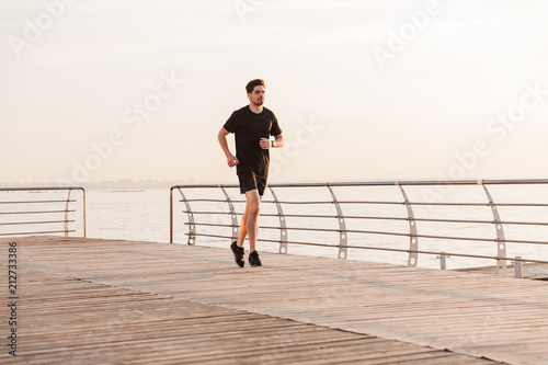 Handsome young sportsman running outdoors listening music