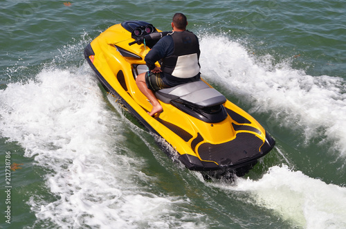 Running waves on a bright yellow jet ski and leaving a wake trail.