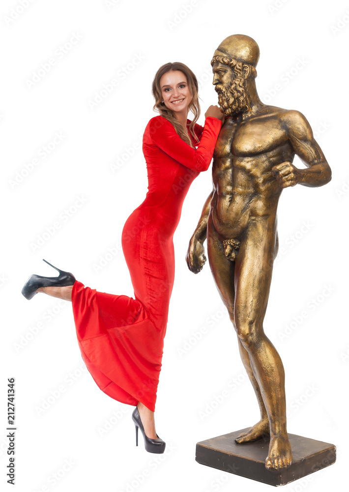 Slender beautiful girl in a red long dress is standing next to a statue on a white background. Slender beautiful girl in a red long dress is standing next to a statue on a white background.