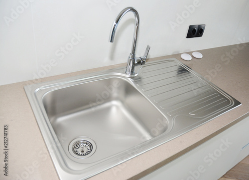 Close up on modern kitchen metal faucet and metal kitchen sink.