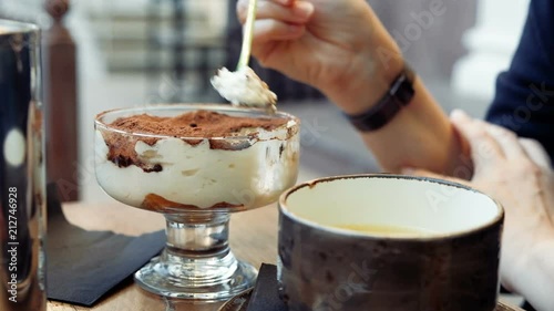 A woman in a cafe is eating a tiramisu cake