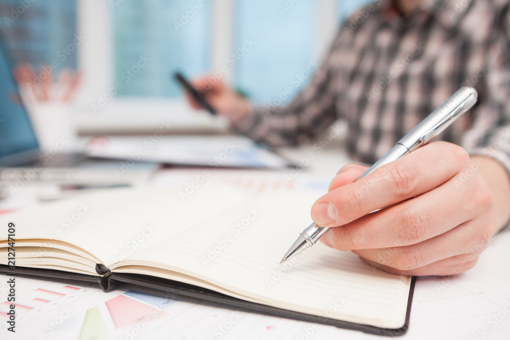 Businessman writes in a notebook while sitting at a desk. Businessman writes in a notebook while sitting at a desk.