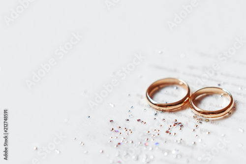 Golden wedding rings on paper invitation with shiny rhinestones. Wedding details, symbol of love and marriage.