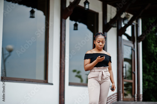 Stylish african american woman posed outdoor and using mobile phone.