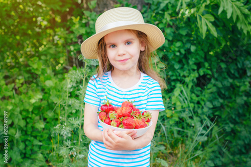 happy baby girl holding a plate of strawberries in her hands.