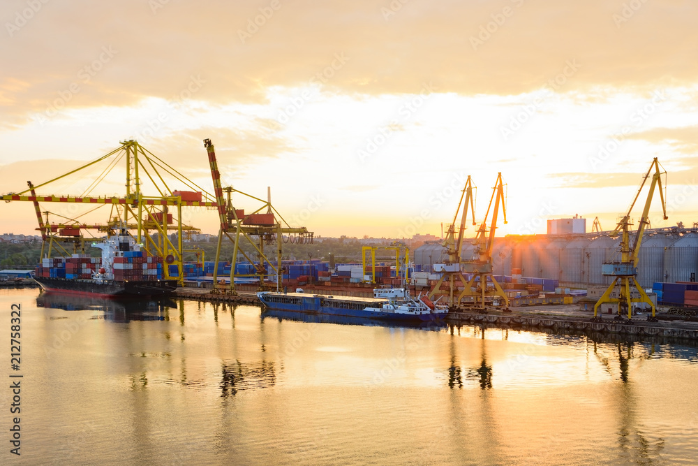 Golden sunset over sea port at summer. Reflections of port facilities and beautiful sky in mirror – like calm water