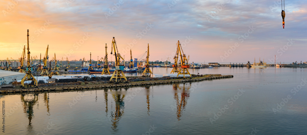 Golden sunset over sea port at summer. Reflections of port facilities and beautiful sky in mirror – like calm water