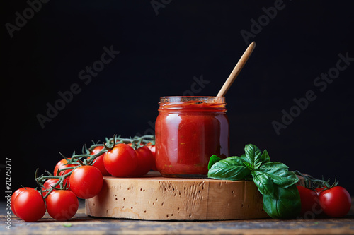 Tomato sauce in a glass jar, tomatoes and herbs on its side.