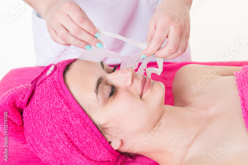 a beautician removes the facial cleansing mask from her client face
