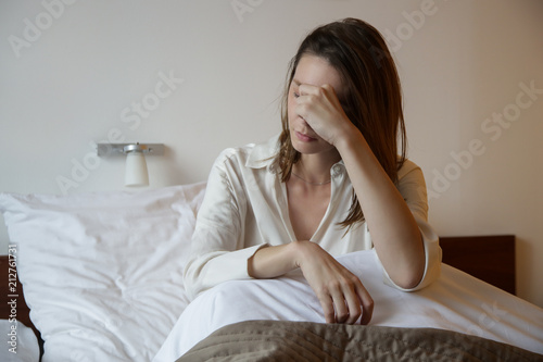 Young woman in the bed covering face with hand, depression, relationship difficulties, migraine or morning sickness concept